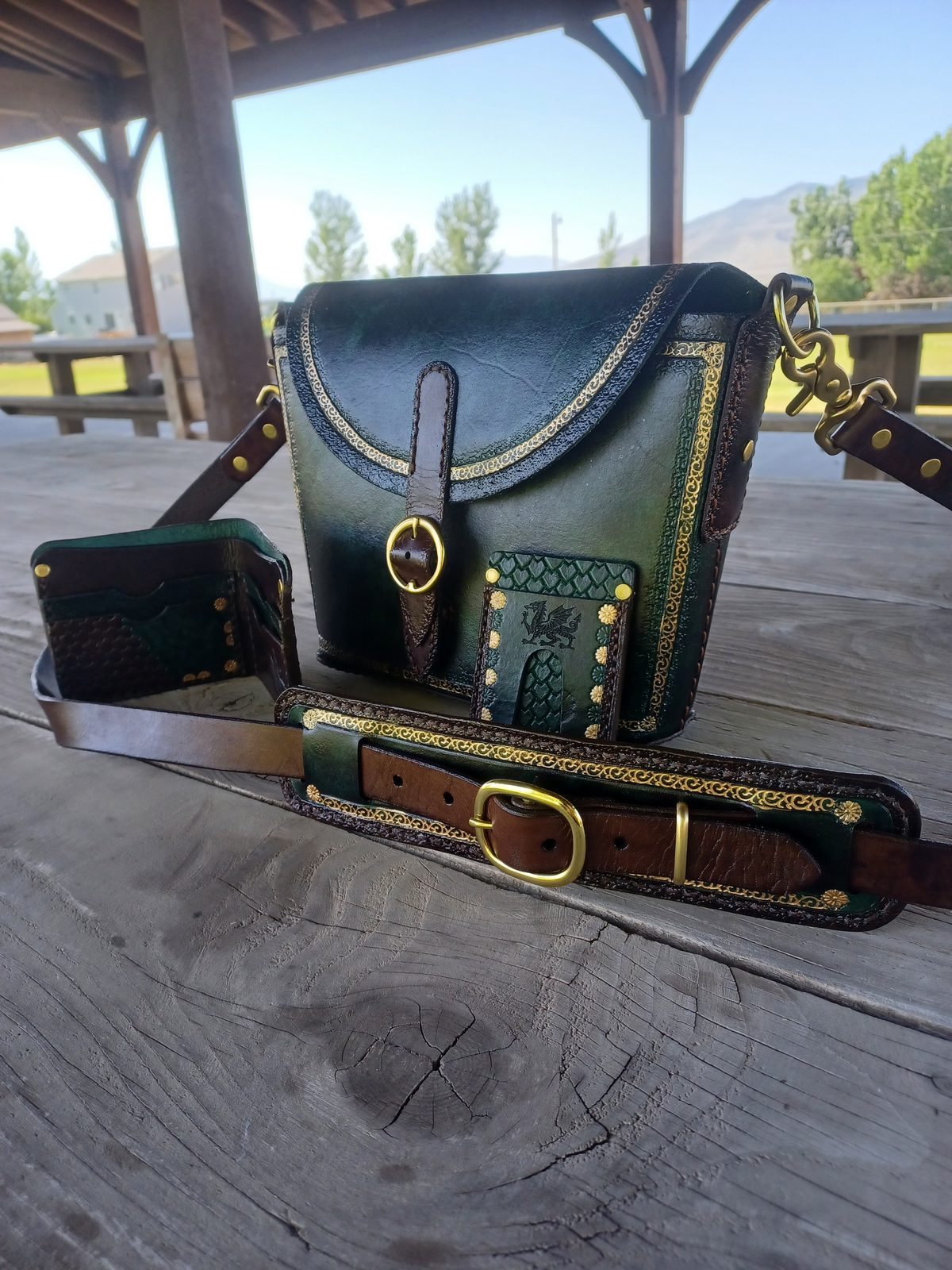 Matched emerald satchel, wallet and belt laid out on a weathered wood table